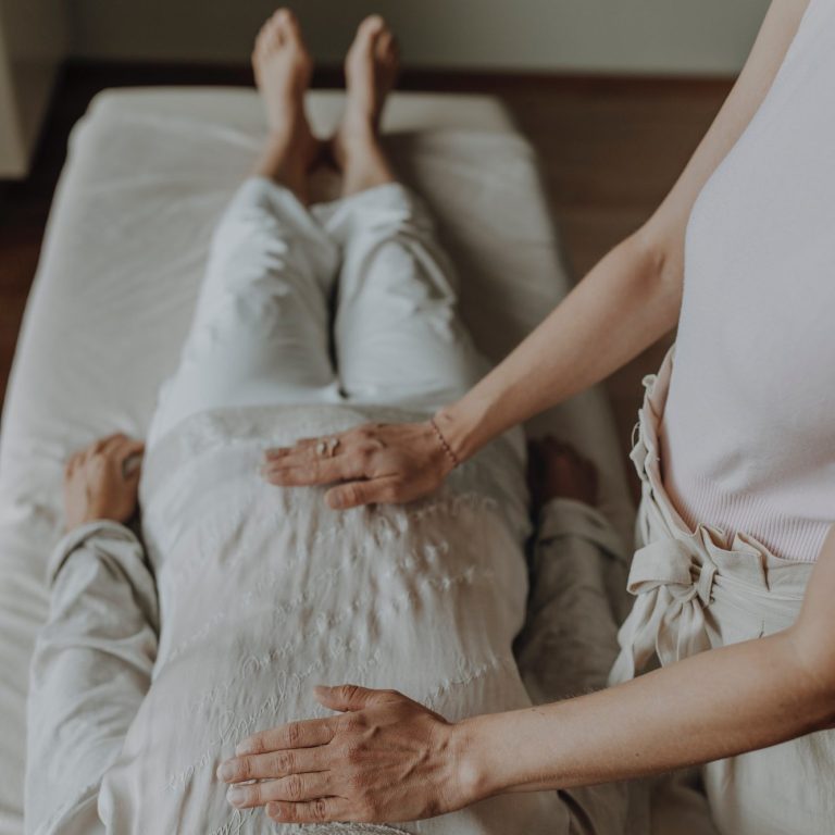 Reikibehandlung Junge Frau hält ihre Hände über eine Frau die auf einer Liege liegt, sie wendet Reiki an