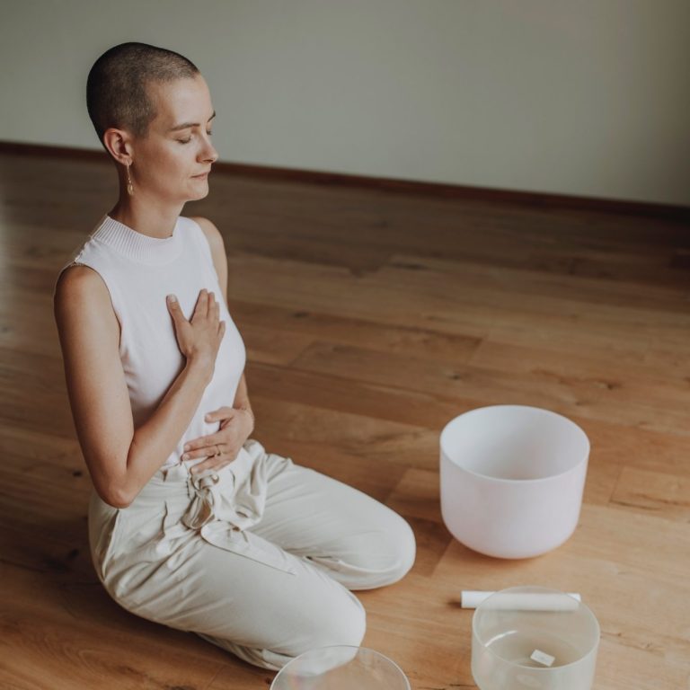 Meditation und Atemübung Eine junge Frau sitzt auf den Knien und meditiert, hält sich dabei Hände auf Brustkorb und den Bauch